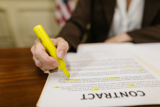 Un'immagine di una persona che evidenzia con inchiostro giallo alcune parti di un contratto legale.