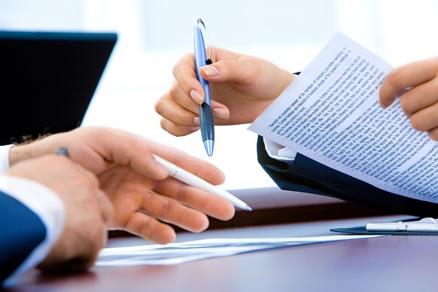 Due mani tengono penne e fogli di carta stampata uno di fronte all'altro su una scrivania.
