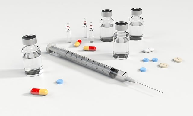 Una siringa, fiale di farmaci, pillole e capsule su una superficie bianca.