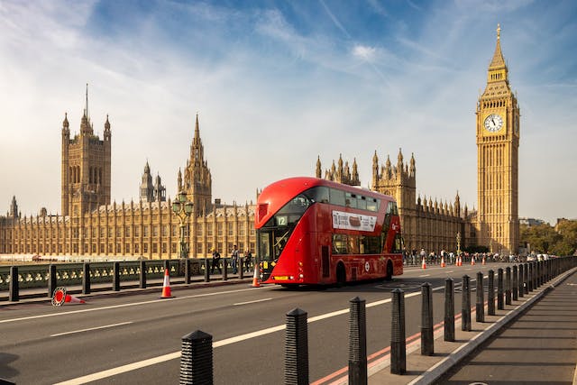 ロンドンの赤い乗り降り自由バスがビッグ・ベンを通過する。