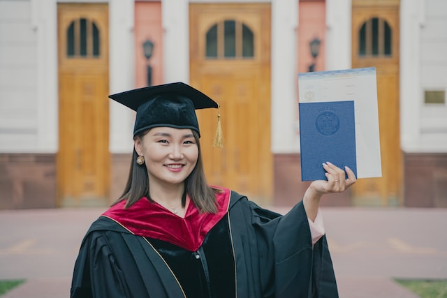 졸업 모자와 가운을 입은 여성이 졸업장을 들고 있다.