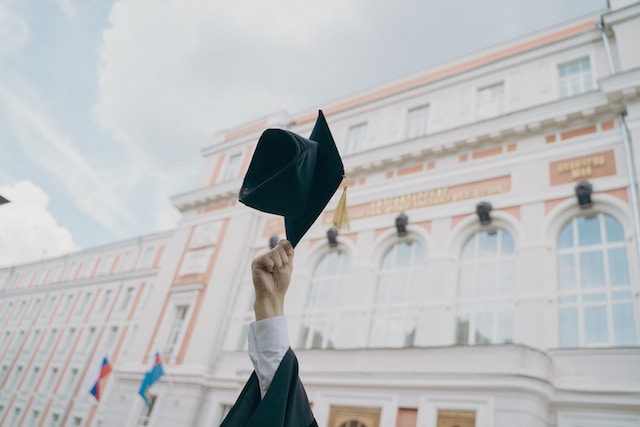 Zdjęcie przedstawiające kogoś kierującego w niebo czapkę z togą akademicką.