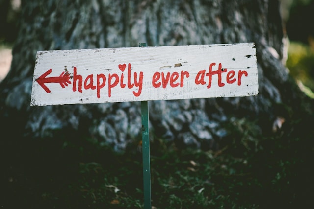 "Happily ever after" napisane na czerwono na białym drogowskazie.
