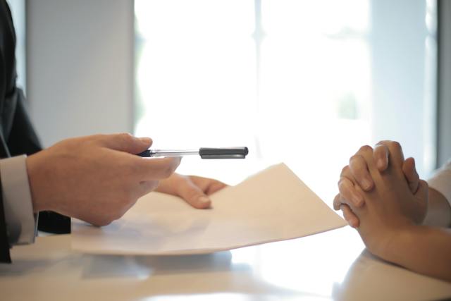 A person handing over a pen and document to another person.
