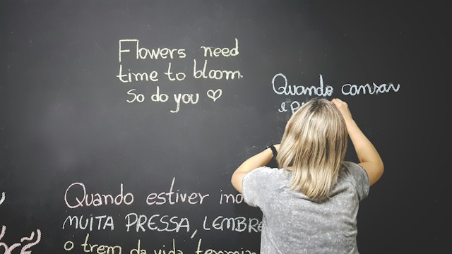 A teacher uses white chalk to write English and Portuguese on a blackboard.
