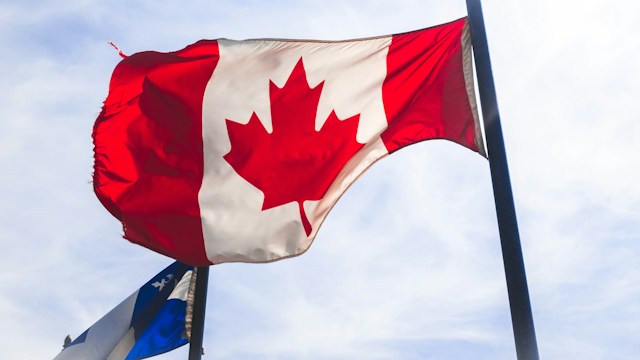 The Canadian flag is waving high in the wind during the daytime.
