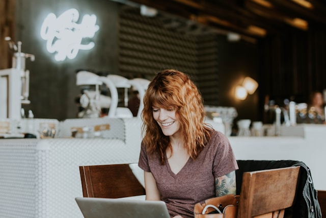 A woman sits on a wooden chair while using a laptop.