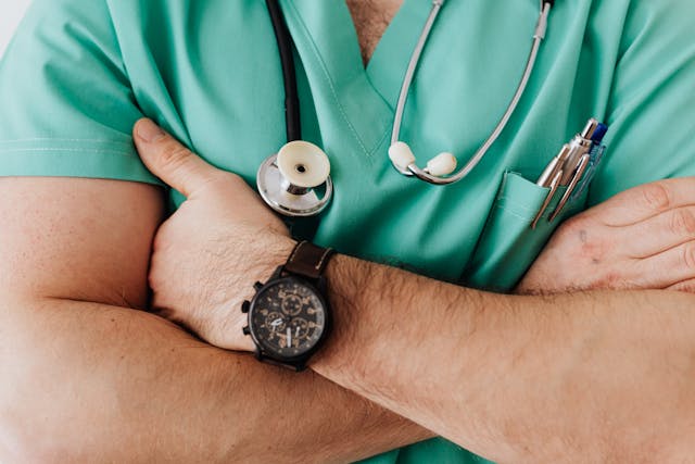 A doctor with a stethoscope on his neck and several pens in his pocket.