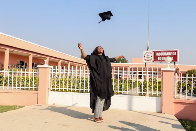 A woman wearing an academic gown tosses her hat.