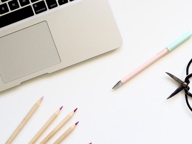 Some pens and a silver laptop are on a white surface.
