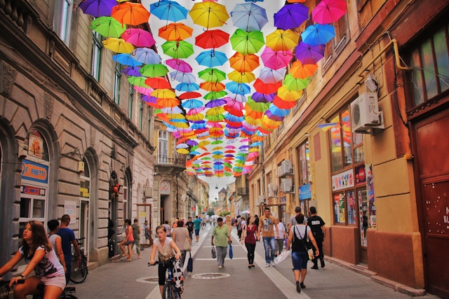 Multiple umbrellas hang over a street as people do business.
