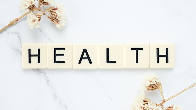 White square marble tiles spell “Health” beside white flowers on a white surface.
