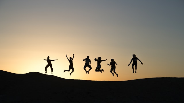 A silhouette of six people jumping behind a sunset.
