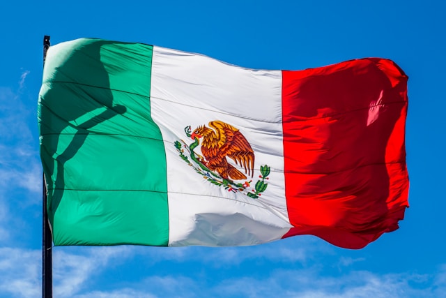 A Mexican flag waves freely in the sky. 
