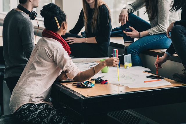 A group of people sit around a table filled with papers and pens.
