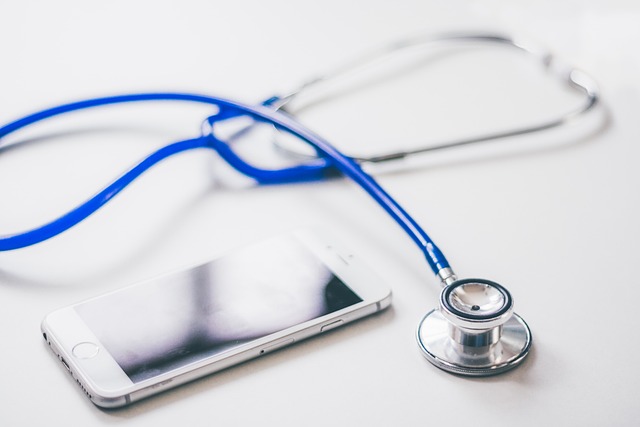 A blue stethoscope is beside a white smartphone on a white surface.
