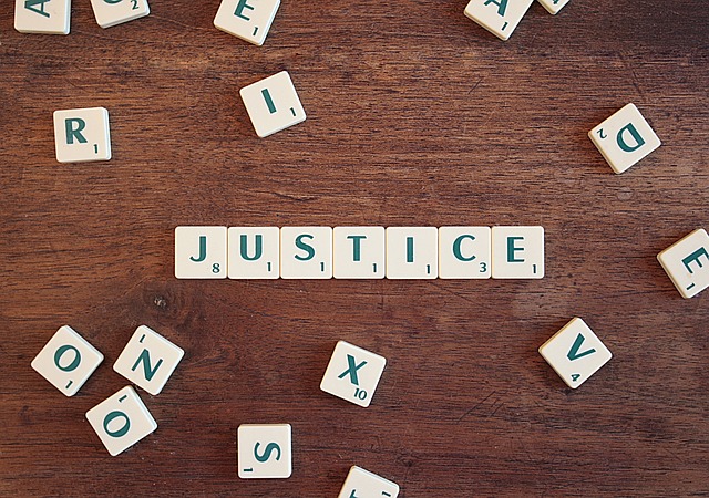 White scrabble tiles spell Justice on a wooden surface.
