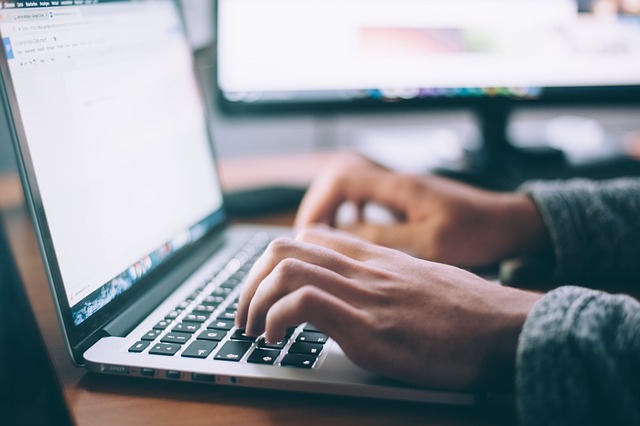 A hand wearing a gray sweater types on a gray laptop.
