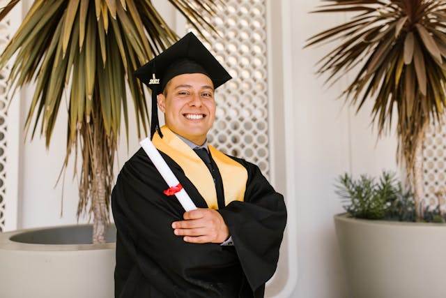 A person in a graduation gown smiles and holds a diploma certificate.
