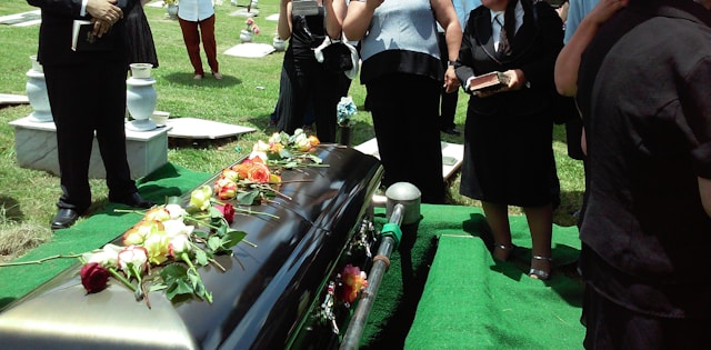 People stand around a coffin with flowers on it.