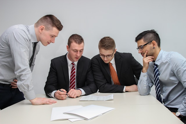 Four people review a handbook on a table.
