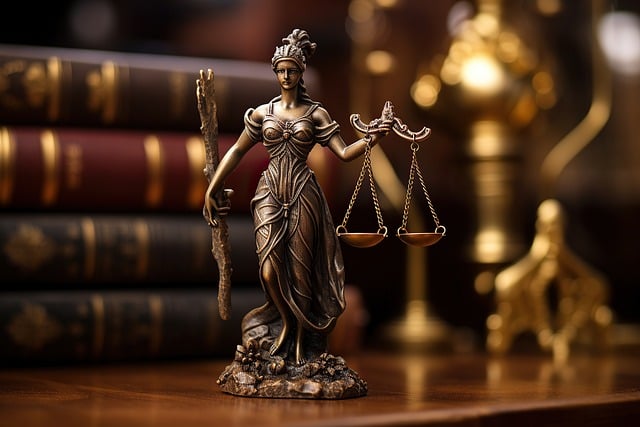 A bronze statue of Lady Justice with a stack of legal books in the background.
