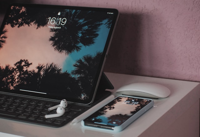 A MacBook, an iPhone, and a pair of airpods on a table.
