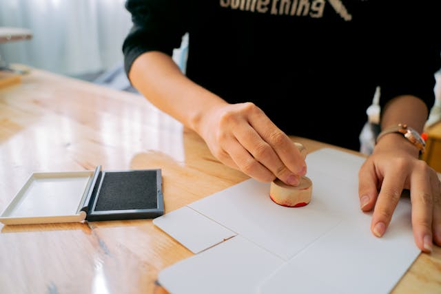 A person stamps a document with a wooden stamp on a table.
