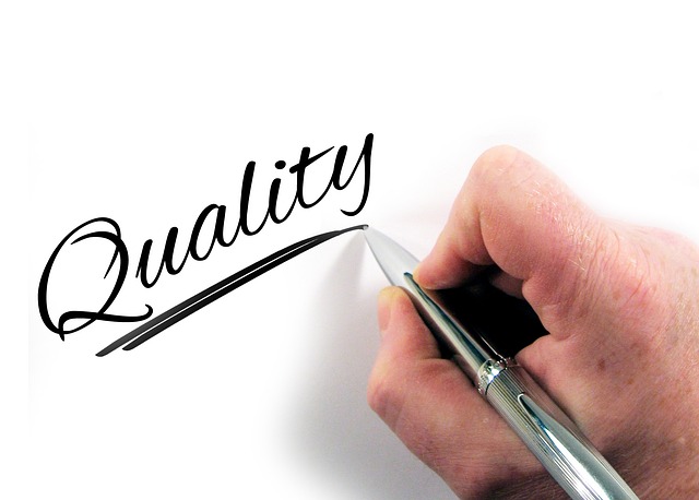 A person writes "Quality" with a pen on a white surface.
