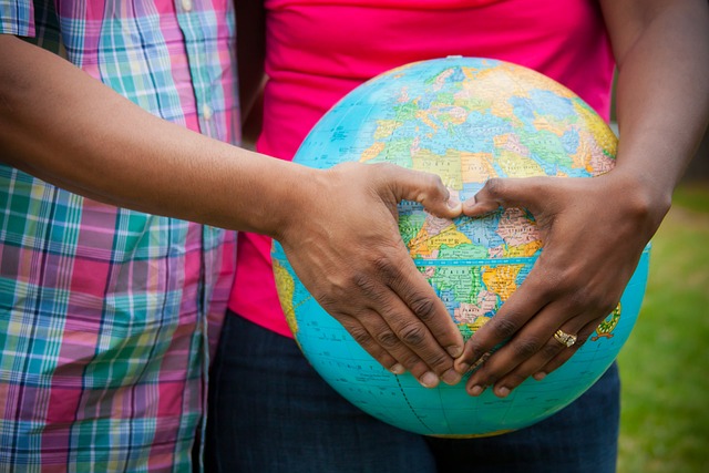 Two people hold a globe while using their hands to create a love symbol.
