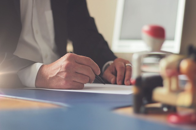 A close-up view of a person wearing a black suit writing in a book.
