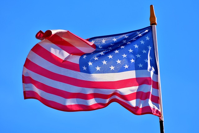 The American flag flutters in the wind on a pole during the day.
