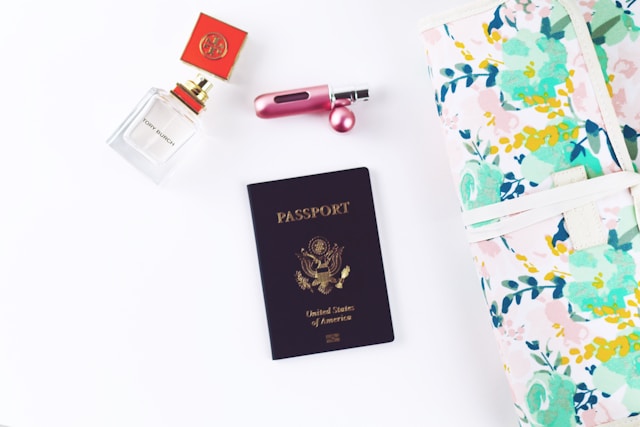 The U.S. passport, a bag, perfume, and lipstick on a white surface.
