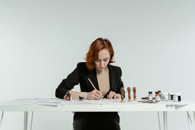 A lady writes on a desk with stamps on the table.
