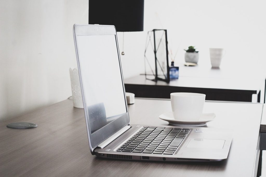 A silver laptop beside a white ceramic teacup on a wooden surface.
